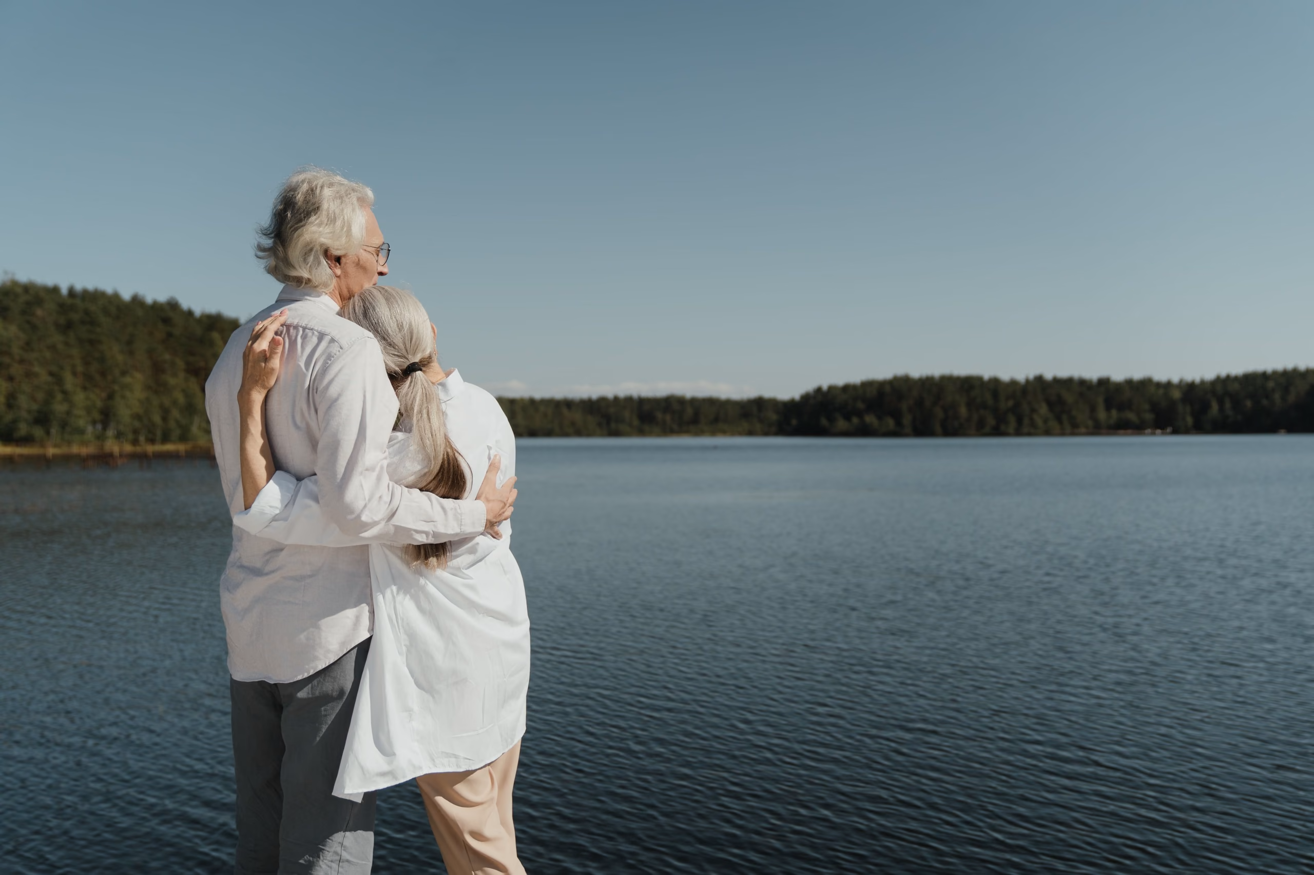An older couple by the water, arm in arm, looking out over the lake