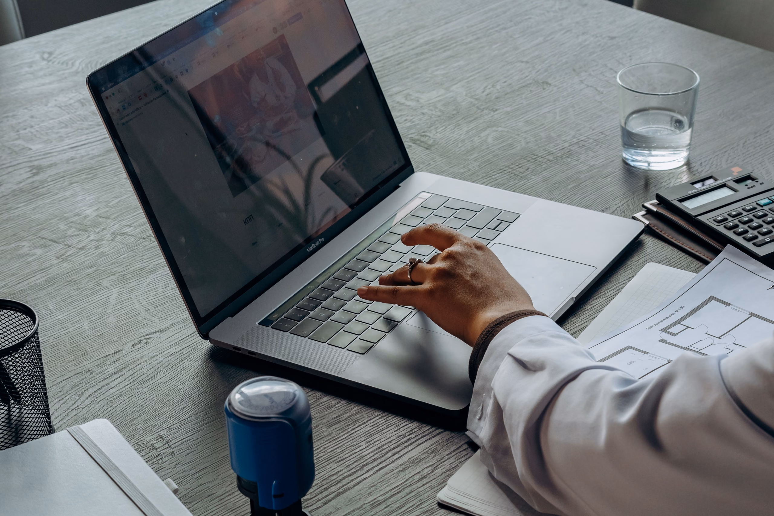A laptop on a desk with a notary stamp, a floor plan and a calculator beside it